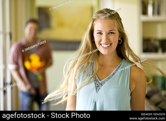 Portrait of young woman turning to face the camera as she is walking towards boyfriend holding a bouquet of flowers