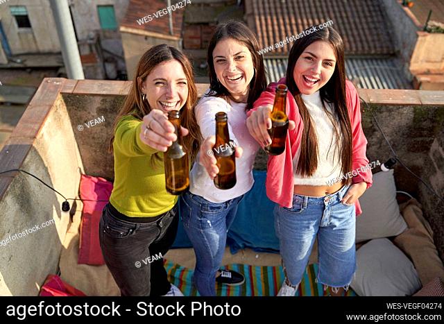 Cheerful female friends raising beer bottle while enjoying on rooftop