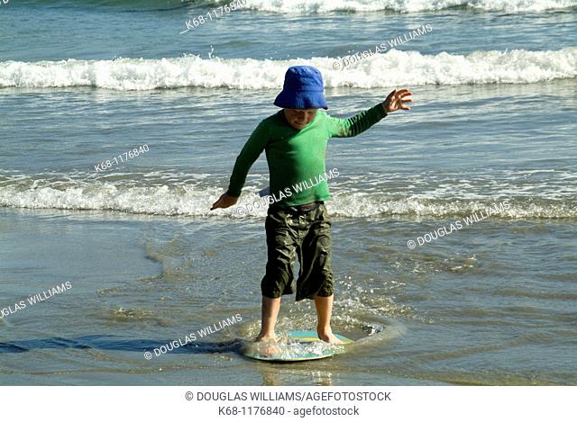seven year old boy playing with a skim board on the beach near Tofino, West Coast, Vancouver Island, British Columbia, Canada