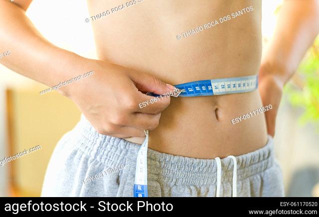 Skinny young woman measuring her slim waist with a measuring tape