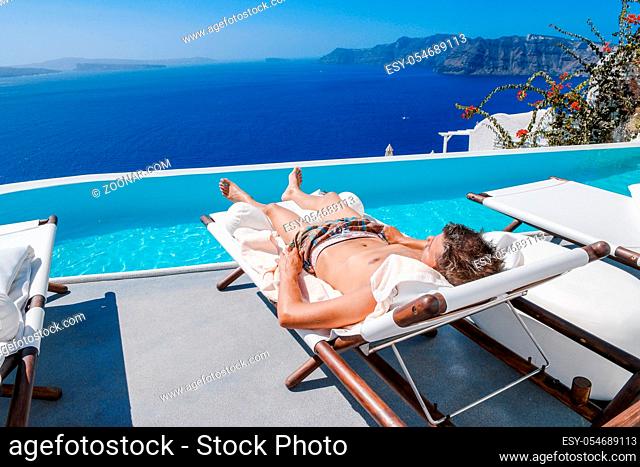 Santorini Greece Oia, young men in swim short relaxing in the pool looking out over the caldera of Santorini Island greece, infinity pool