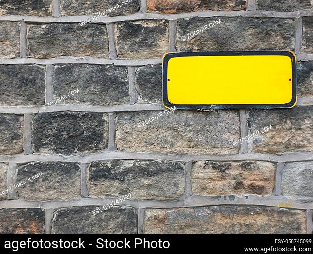 a blank yellow metal sign with empty space for copy text on an old stone wall background