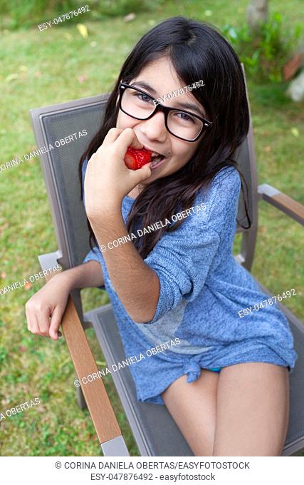 Cheerful Caucasian girl in the garden, biting a strawberry