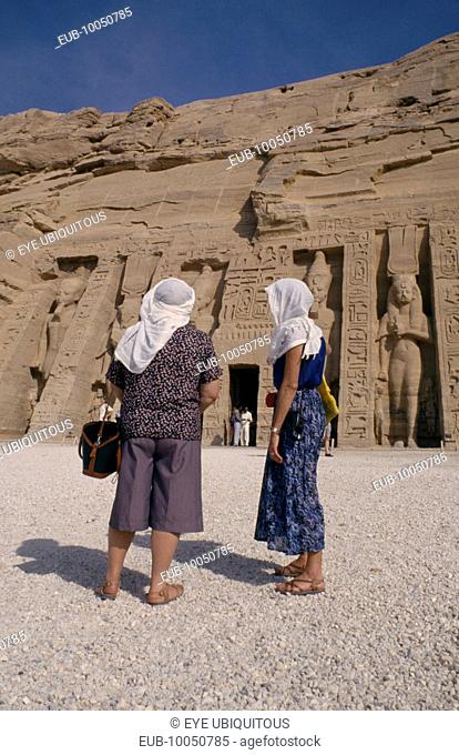 Two female tourists wearing head scarves in front of staues of Ramesses II at the temple entrance