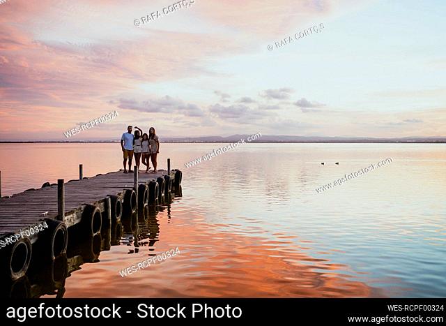 Family standing at jetty against sky during sunset