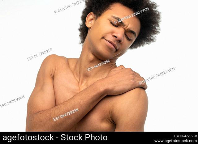 Painful. Curly-haired young guy suffering from pain in his shoulder