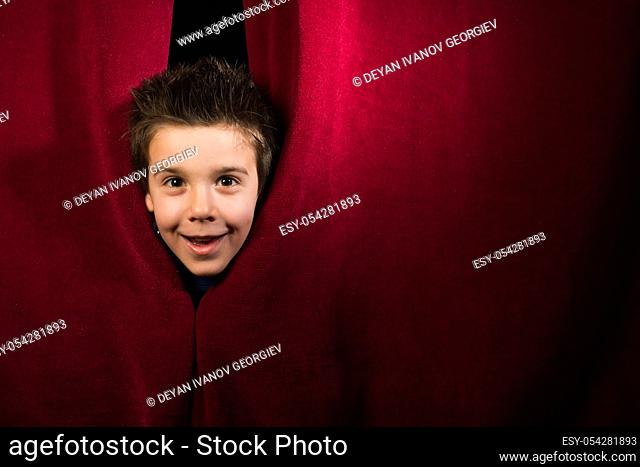 Child appearing beneath the curtain. Red curtain