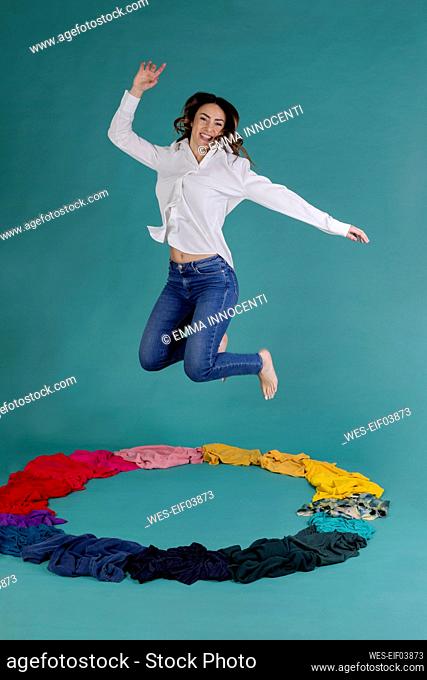 Happy woman jumping over clothes against blue background
