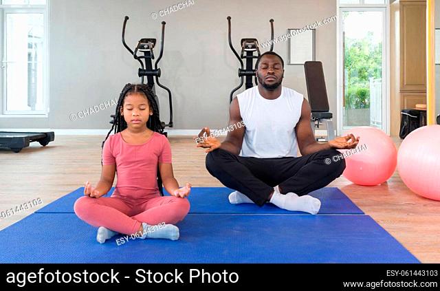 ?Black Cornrow Braids girl in sportswear meditating with her father on yoga mat before exercise. Two yoga ball are placed next to them