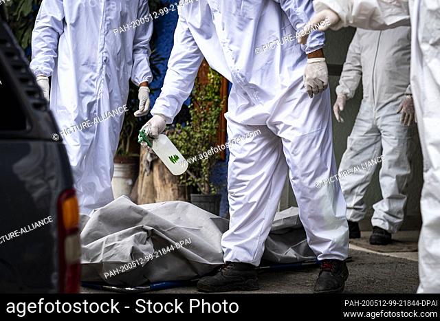 11 May 2020, Mexico, Mexiko-Stadt: Employees of a funeral director spray disinfectant on the body of a Covid 19 victim in front of the Xilotepec crematorium