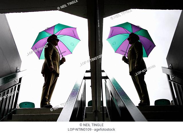 England, London, Wimbledon, A Service Steward and his umbrella is reflected in a glass pane in one of the entrances to centre court at the Wimbledon Tennis...