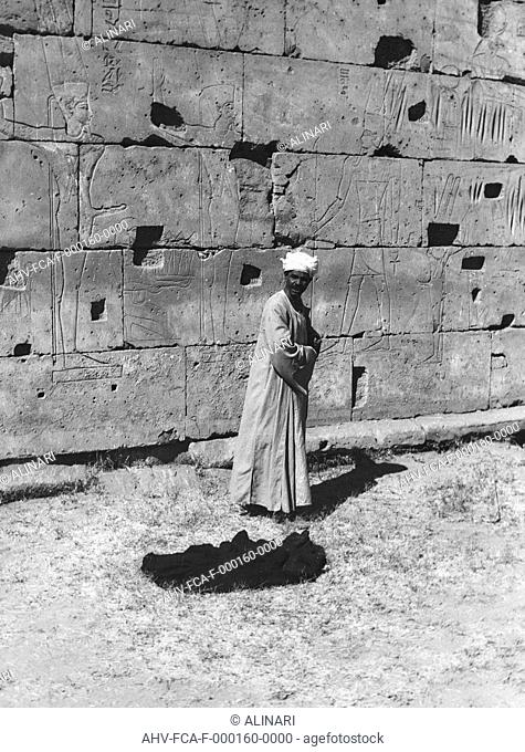 Man portrait near a wall engraved with figures of deities, Egypt, shot 1950-1960 by Clerici Fabrizio