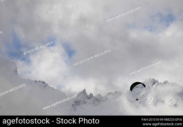 dpatop - 18 October 2020, Bavaria, Garmisch-Partenkirchen: A paraglider flies past the snow-covered peaks of the Wetterstein mountain range
