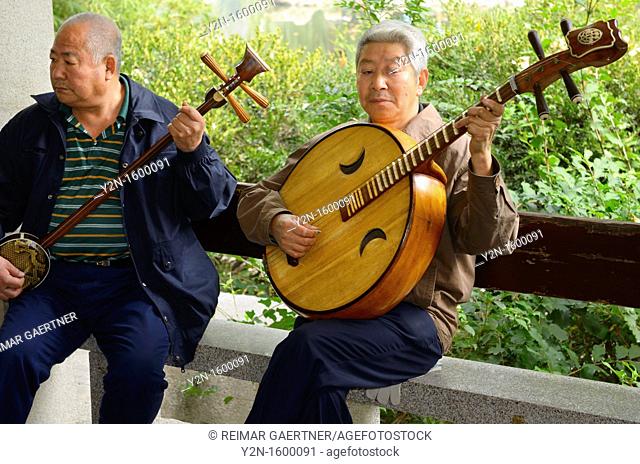 Two men playing a Chinese banjo and Ruan in an orchestra outdoors at Zizhuyuan Purple Bamboo Park in Beijing