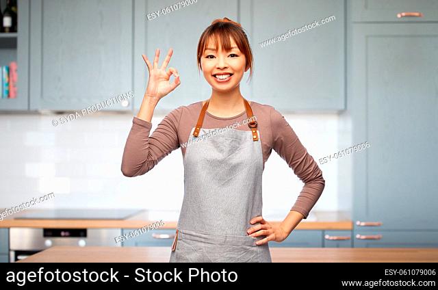 happy woman in apron showing ok gesture in kitchen