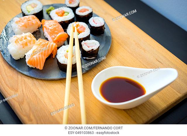 Maki on a wooden table on black slate plate with soy sauce and chopsticks