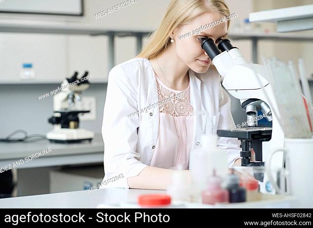 Blond female scientist researching through microscope in laboratory