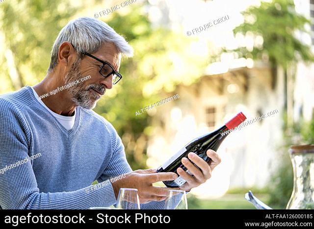 Mature man looking at wine bottle while sitting on chair