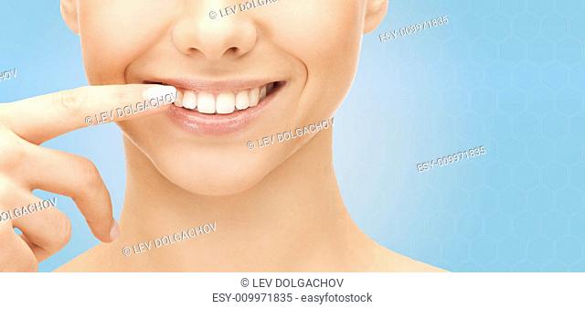 dental health, beauty, hygiene and people concept - close up of smiling woman face pointing to teeth over blue background
