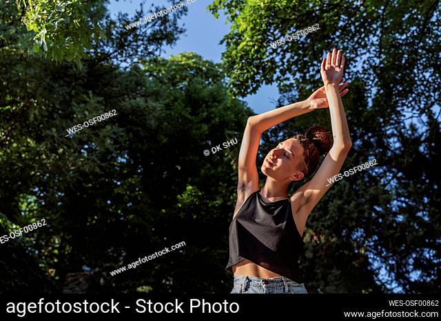 Non-binary person enjoying sunlight with arms raised