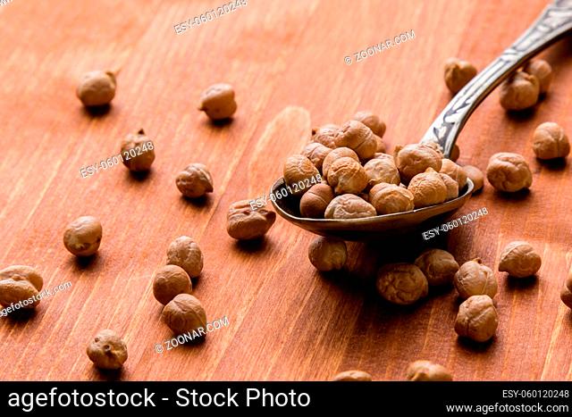 dry brown chickpeas on wooden table with spoon