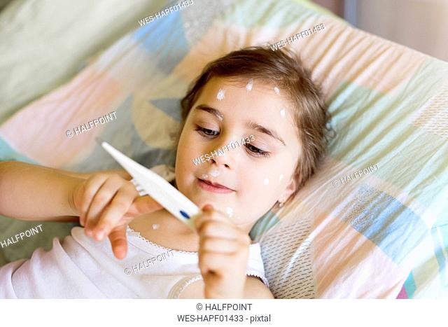 Girl having chickenpox lying in bed looking at clinical thermometer