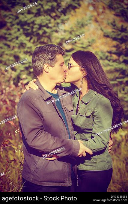 A mature married couple holding each other and kissing in a park during the fall season; St. Albert, Alberta, Canada