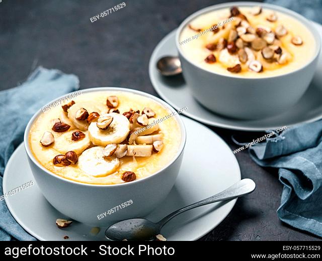 Two bowl with corn semolina porridge with banana, hazelnut and burnt butter honey.Sweet polenta or cornmeal porridge on black tabletop