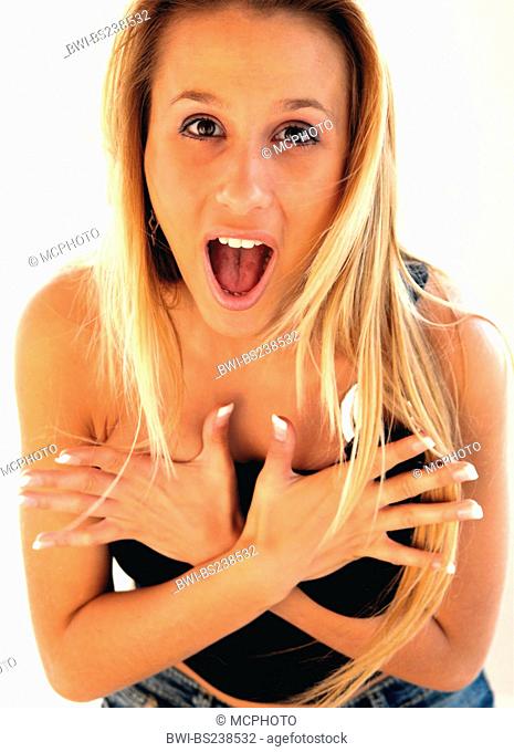 blonde young woman opens her mouth widely of surprise, forgets that she is wearing a top and covers her breast with her hands