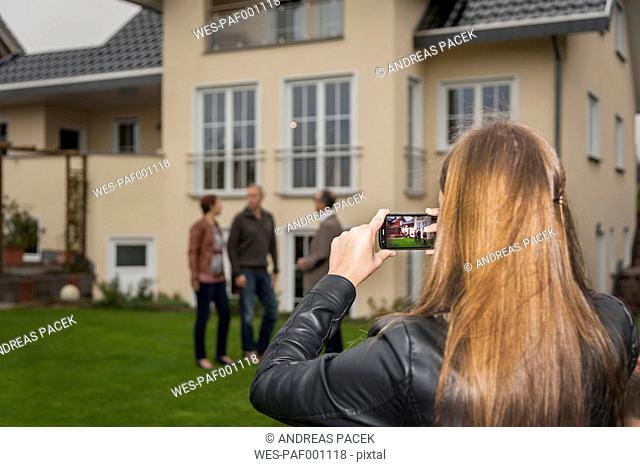 Teenage girl photographing her parents and estate agent in front of residential house
