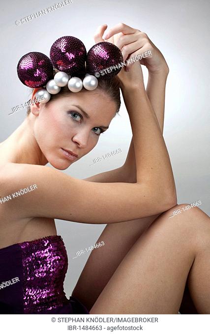 Portrait of a young woman, Christmas balls as hair ornaments, purple, sequined top, direct look