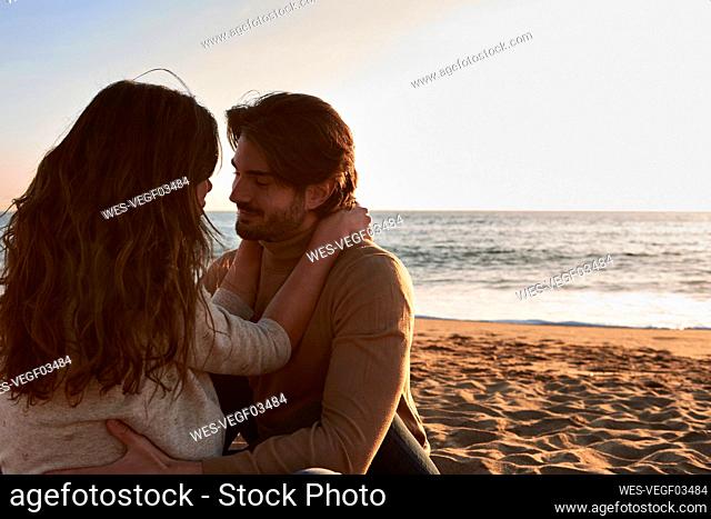Girlfriend and boyfriend with arm around sitting face to face on beach