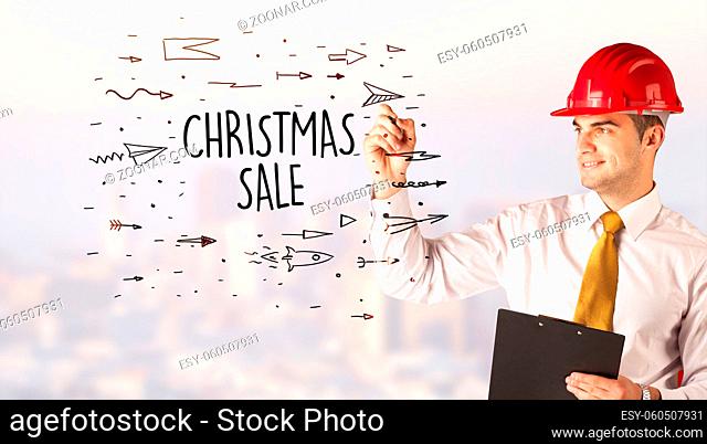 Handsome businessman with helmet drawing CHRISTMAS SALE inscription, contruction sale concept