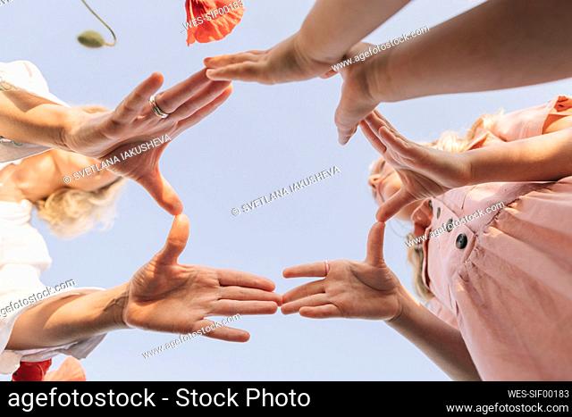 Playful mother with daughters joining fingers under blue sky