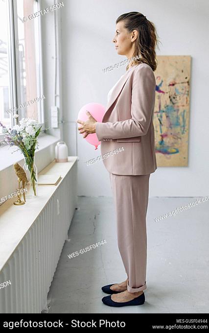 Businesswoman holding balloon in front of stomach in office