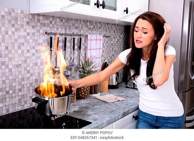 Shocked Young Woman Looking At Cooking Pot Burning With Fire On Induction Stove