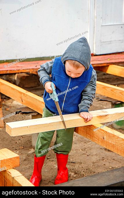Little studious boy sawing a wooden board. Home construction. Little Helper. Little builder