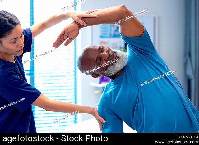 Diverse female physiotherapist treating senior male patient with stretching exercise, copy space