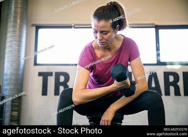 Serious female athlete lifting dumbbell while sitting in gym