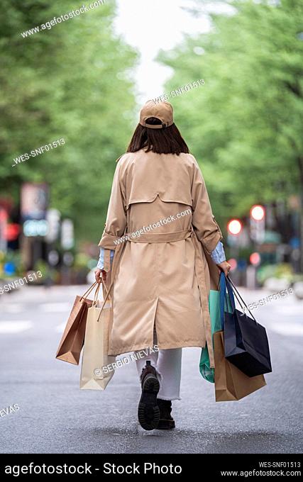 Young woman holding shopping bags while walking on road