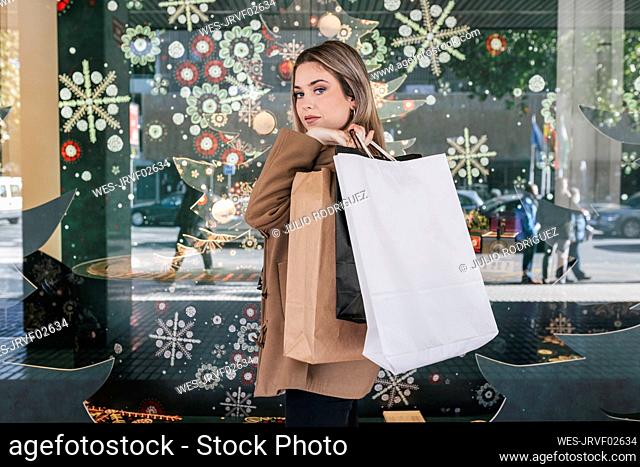 Confident woman with shopping bags by store window at Christmas