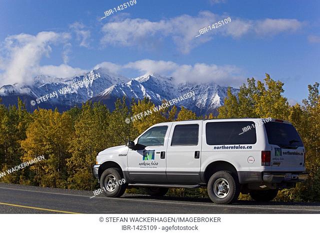 SUV driving along Alaska Highway, Indian Summer, trees in fall colours, St. Elias Mountains behind, Kluane National Park and Reserve, Yukon Territory, Canada