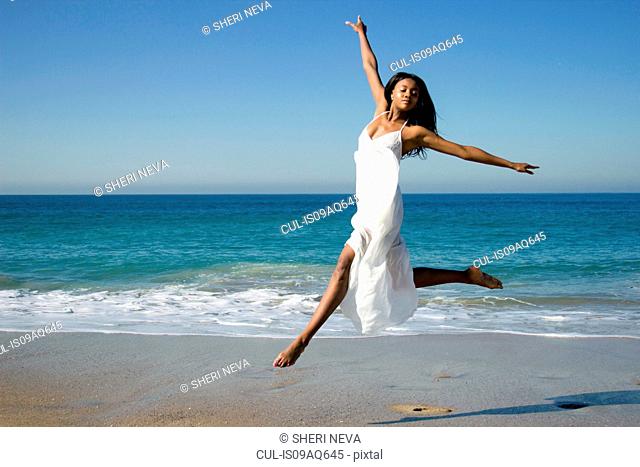 Young female dancer leaping mid air on beach