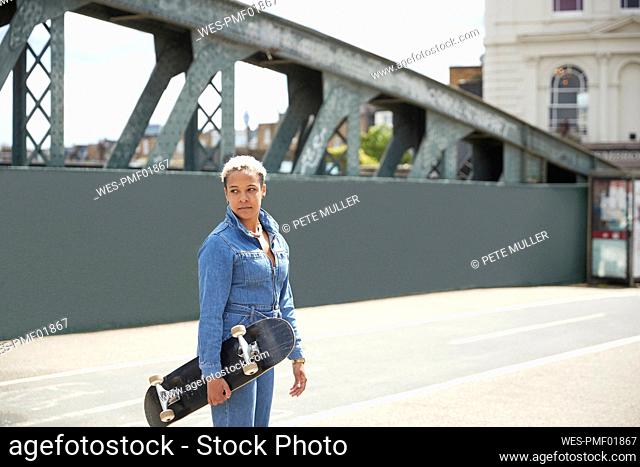 Woman looking away while holding skateboard on sunny day