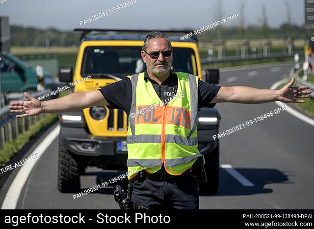 21 May 2020, Schleswig-Holstein, St. Peter Ording: A police officer stops traffic on a country road just before St. Peter Ording