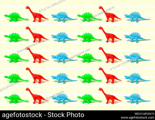 Pattern of green, red and blue plastic dinosaur figurines flat laid against yellow background