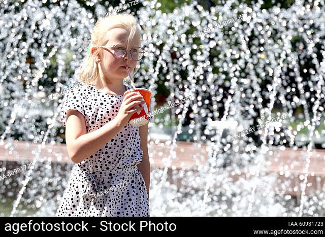 RUSSIA, MOSCOW - AUGUST 7, 2023: A girl with a drink walks past a fountain in Novopushkinsky Garden in summer. Valery Sharifulin/TASS
