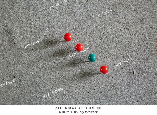 One green and three red circular pushpins pinned onto a bulletin board