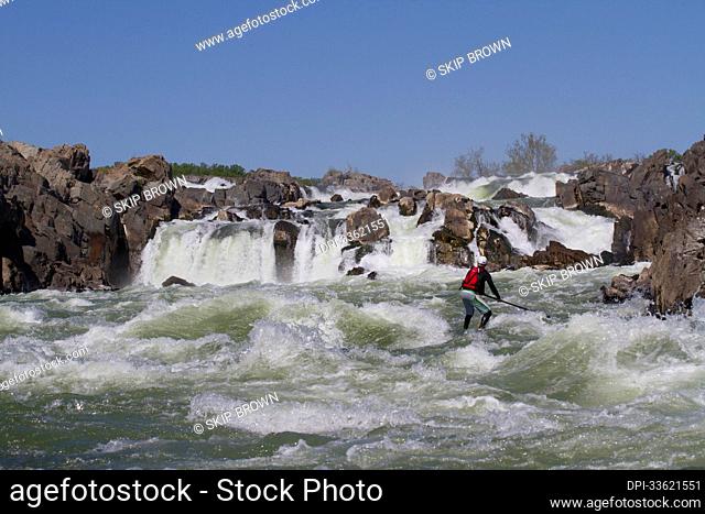 A stand up paddle boarder surfs in white water just below Great Falls.; Potomac River, Maryland/Virginia