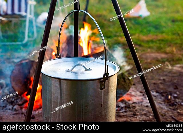 a camping cooking pot hanging over a campfire on a tripod at a tourist camp